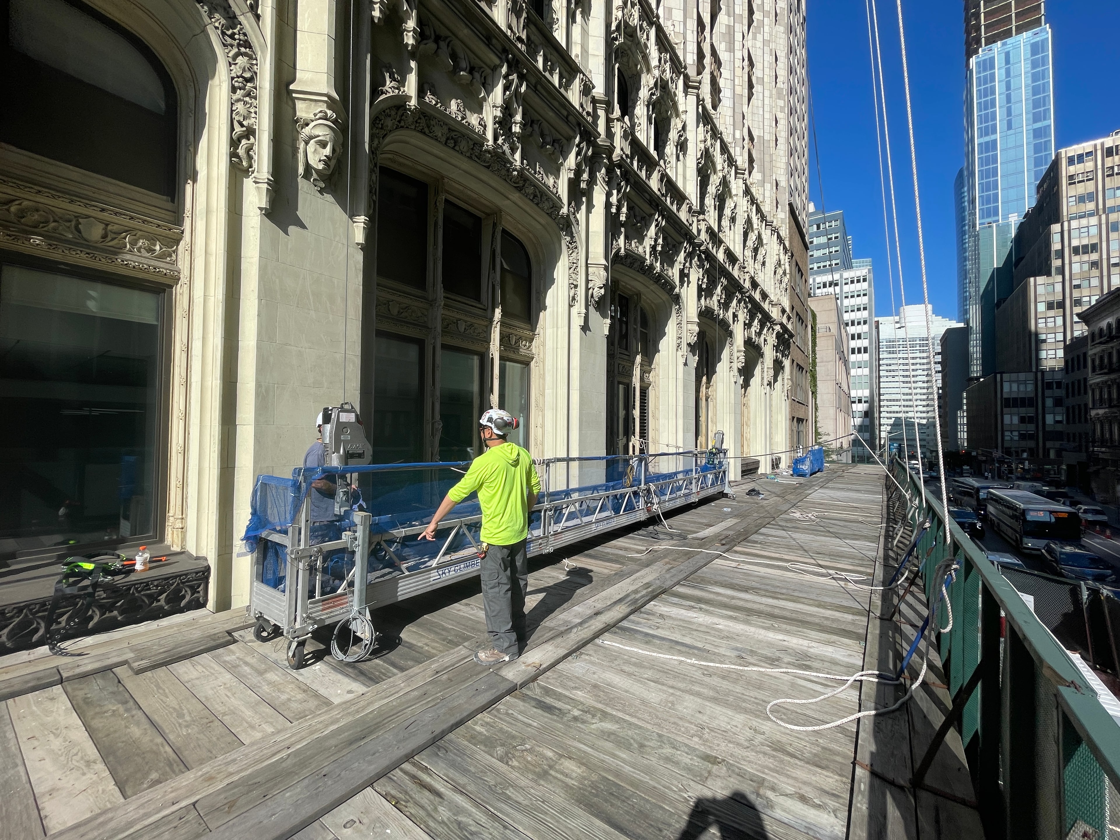Workers and suspended scaffold equipment alongside the Woolworth Building facade